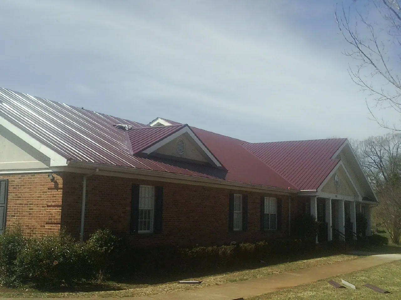 Red metal roof with gabled entries on a long brick building, from a Hail Damage Roof Repair job in Steubenville