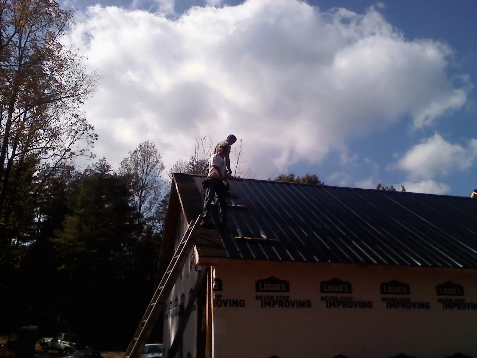 Roofer fastening dark metal panels high against a cloudy sky, from a Roof Inspection job in Steubenville