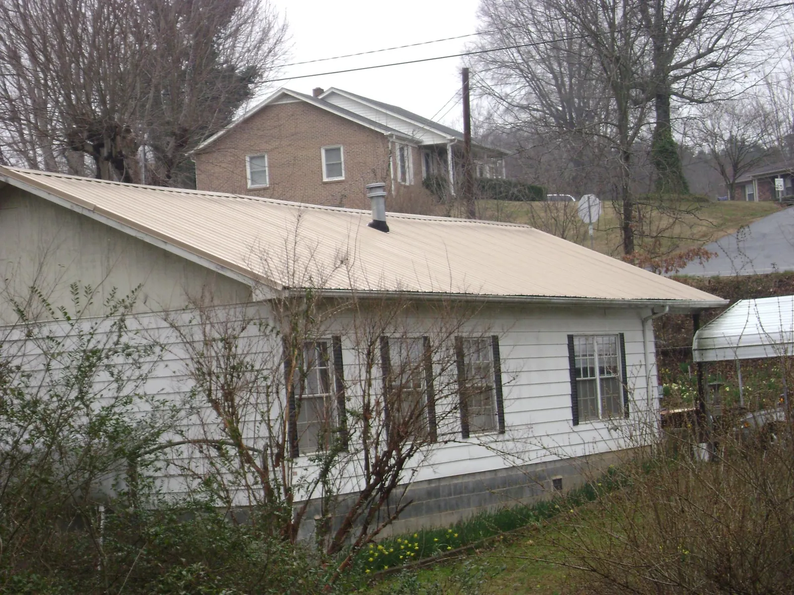 Tan metal roof on a white sided house set into a hillside — Commercial Roofing by Roofing Brothers in Steubenville